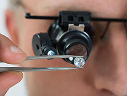 man looing through a loop at a diamond held in a pair of tweesers